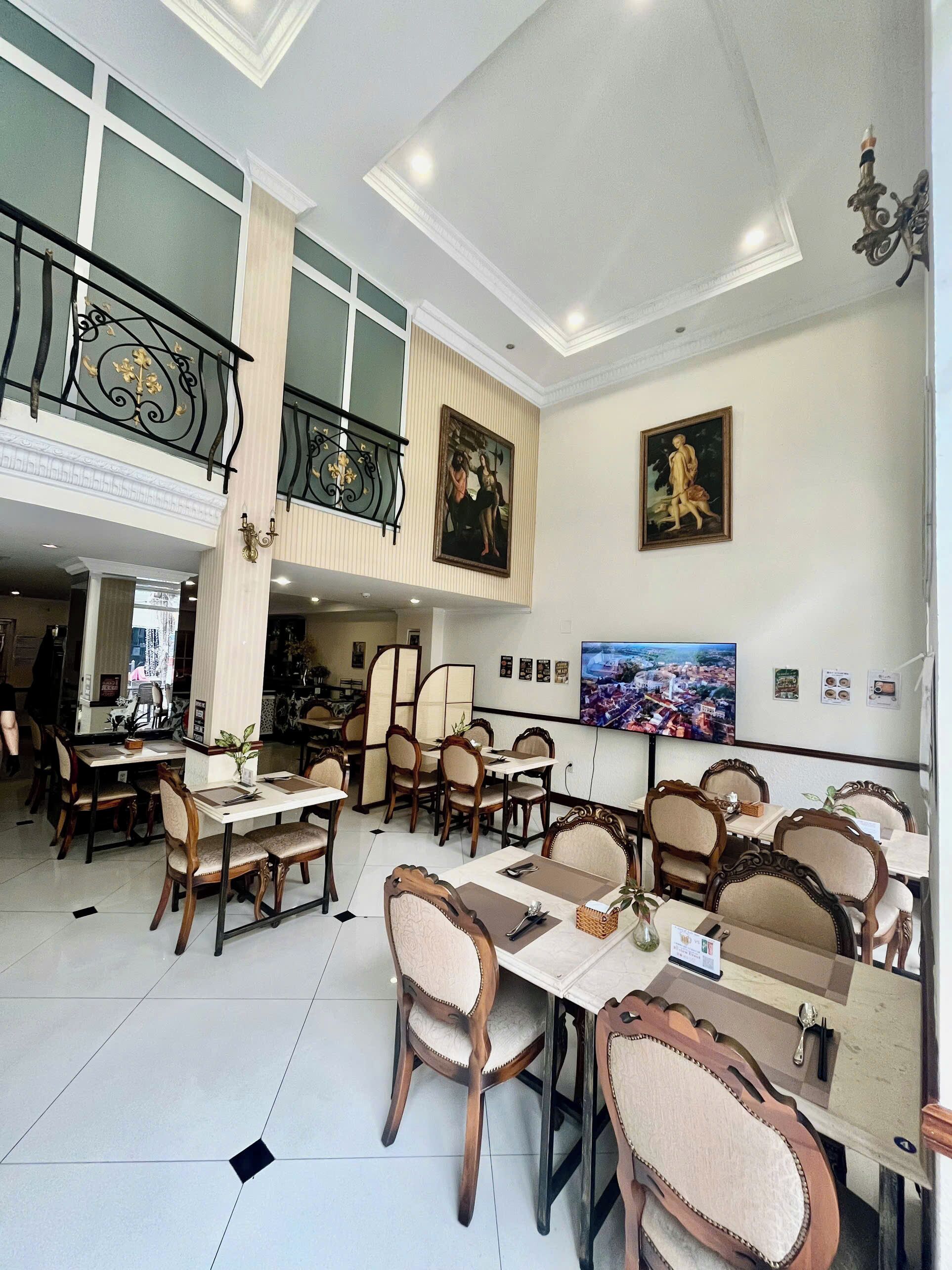 A dining area with multiple tables and chairs, a balcony with a railing, and artwork on the walls.
