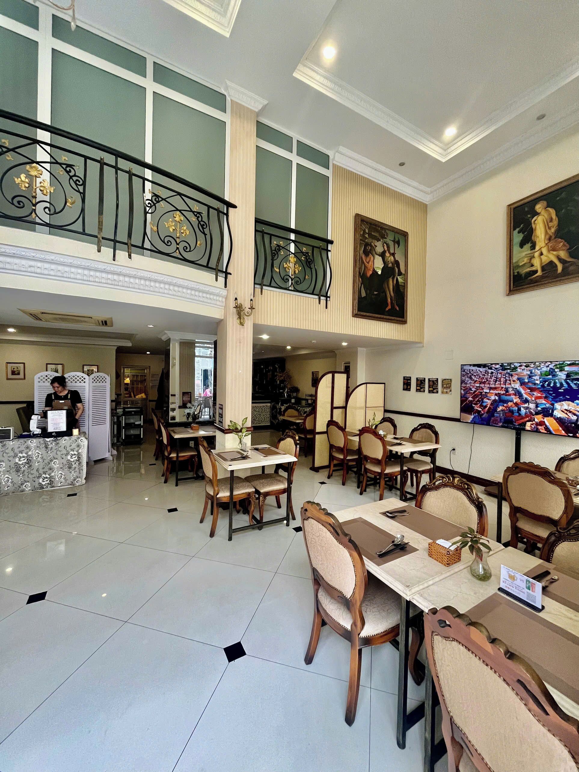 A spacious dining area with high ceilings, a balcony with ornate railings, and artwork on the walls.