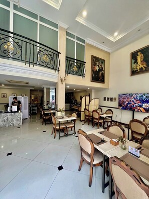 Une salle à manger spacieuse avec de hauts plafonds, un balcon doté de balustrades décoratives et des œuvres d’art aux murs.