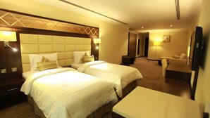A hotel room with two beds, a desk, a chair, and a TV.