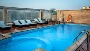 A rooftop pool with lounge chairs and a glass enclosure.
