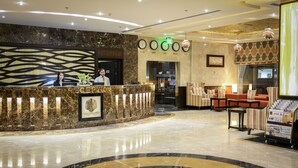 A hotel reception area with a marble counter, clocks, and seating.