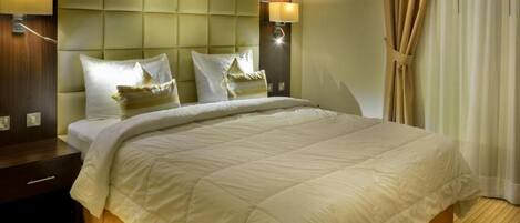 A hotel room with a large bed, a padded headboard, two bedside lamps, and a wooden nightstand.