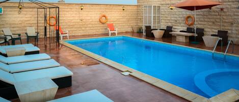 A swimming pool with lounge chairs and umbrellas, surrounded by a stone wall.