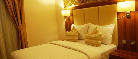 Una habitación de hotel con una cama grande, dos lámparas de noche, un cabecero de madera y una mesita de noche.