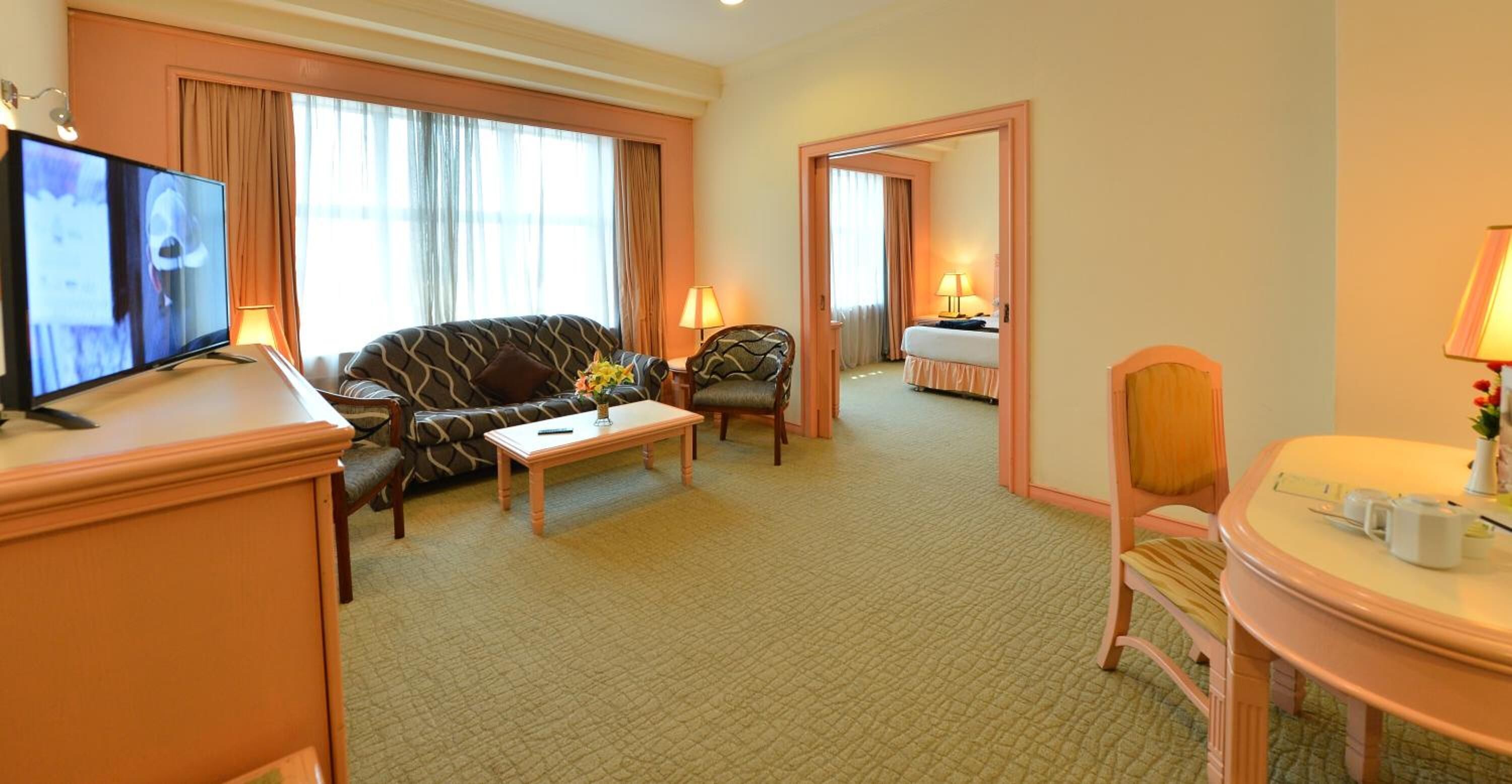 A hotel room with a sofa, a coffee table, a TV, a desk, and a bathroom.