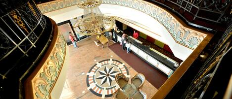 A grand, ornate interior with a central chandelier, a circular floor design, and a seating area.
