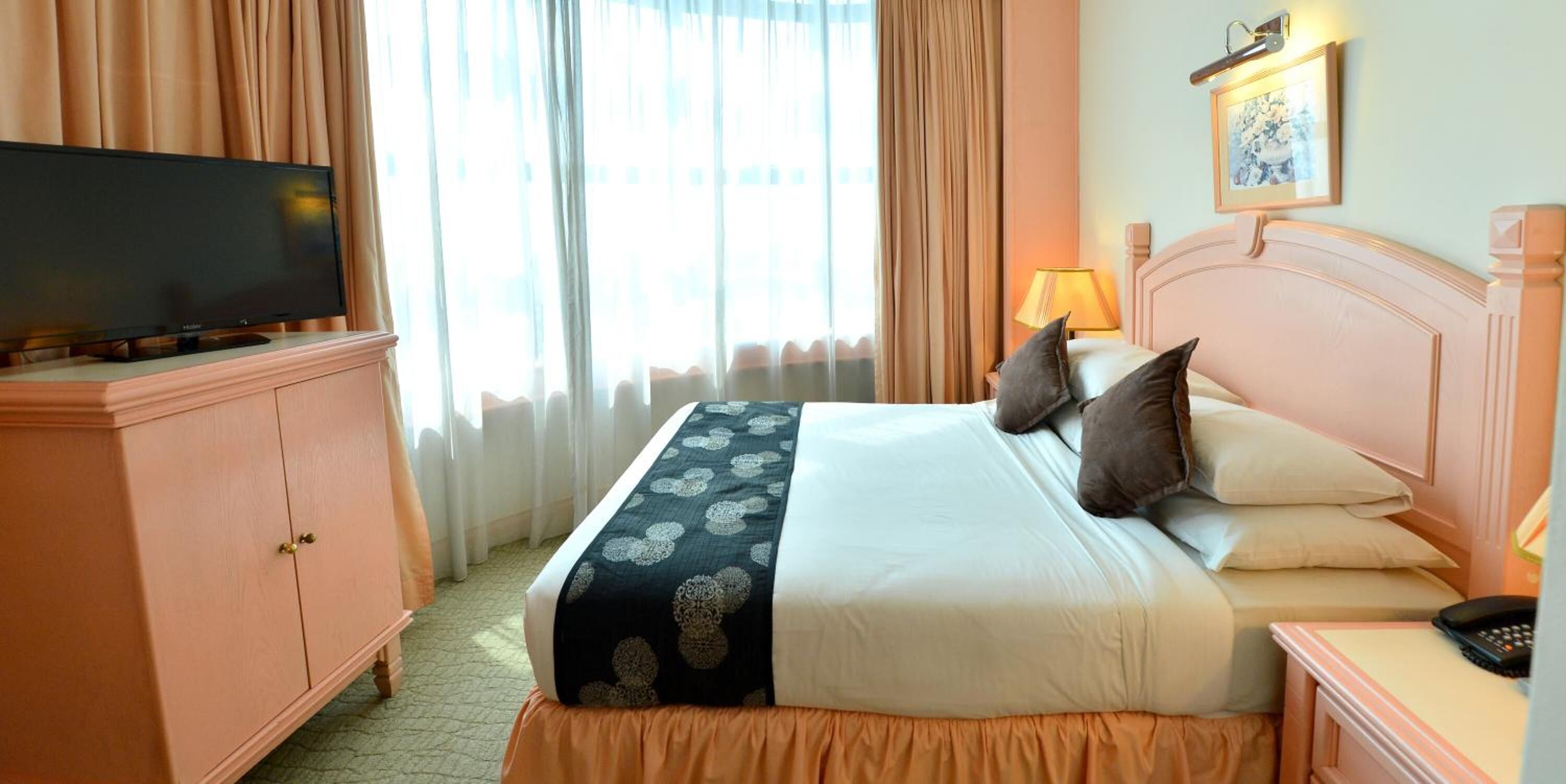 A hotel room with a bed, a television on a cabinet, a bedside table with a lamp, and a framed picture on the wall.