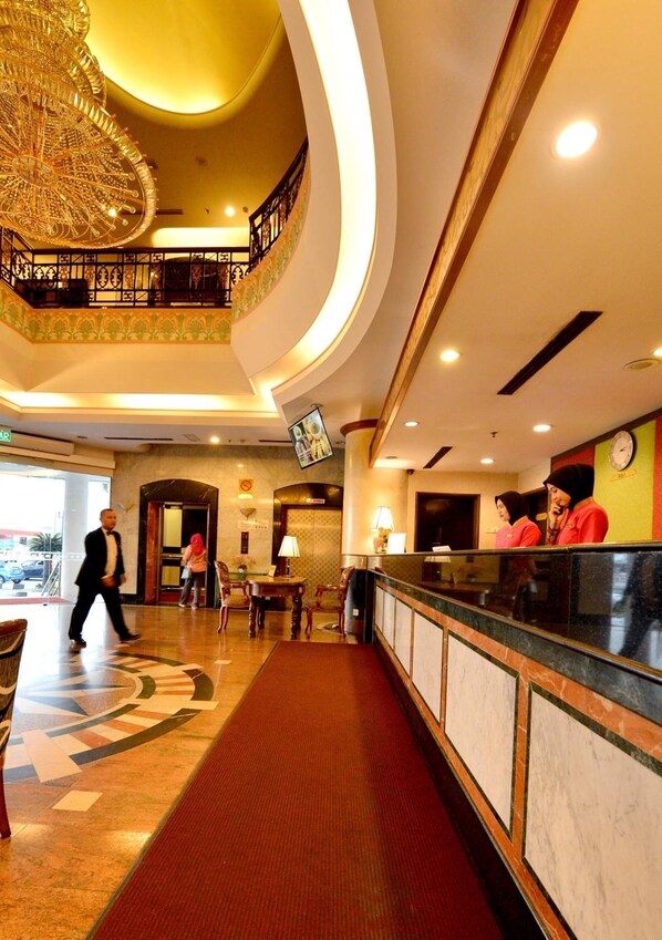 A hotel lobby with a grand chandelier, a reception desk, and a staircase leading to an upper level.