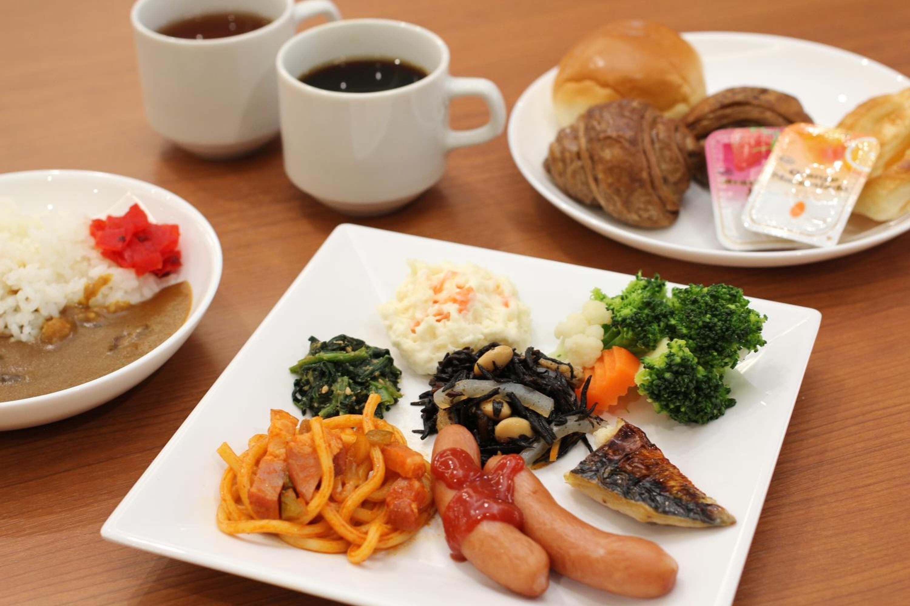 Un repas composé de riz, de légumes et de viande, accompagné de deux tasses de café, le tout servi sur une table en bois.