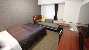 Una habitación de hotel con cama, sofá, escritorio pequeño y televisor.