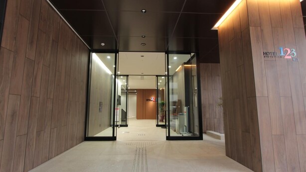 Entrada moderna de hotel con paneles de madera, puertas de vidrio y un letrero que indica la habitación número 123.