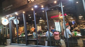 Un restaurante interior con techo de madera y ventanas de vidrio. Las mesas están dispuestas con diversos platos y bebidas.