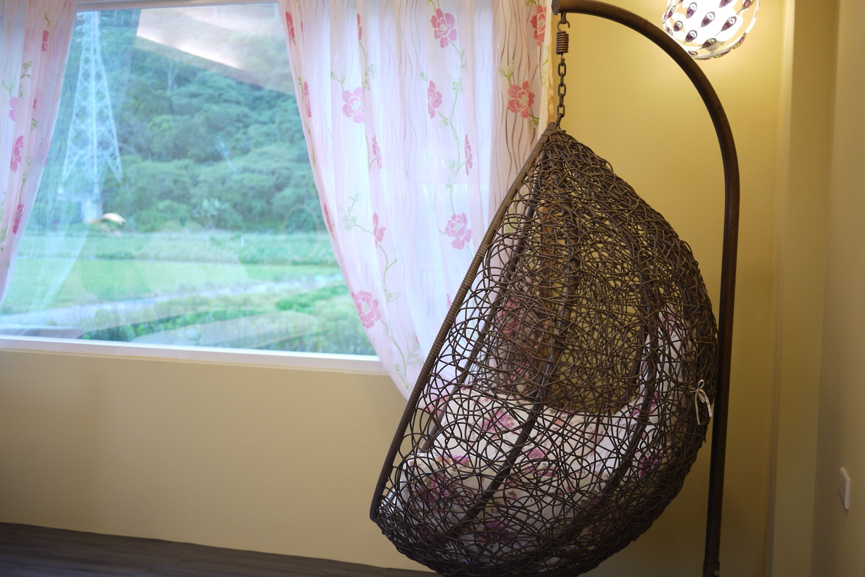 Una hamaca colgante junto a una ventana con cortinas florales y vistas a zonas verdes.