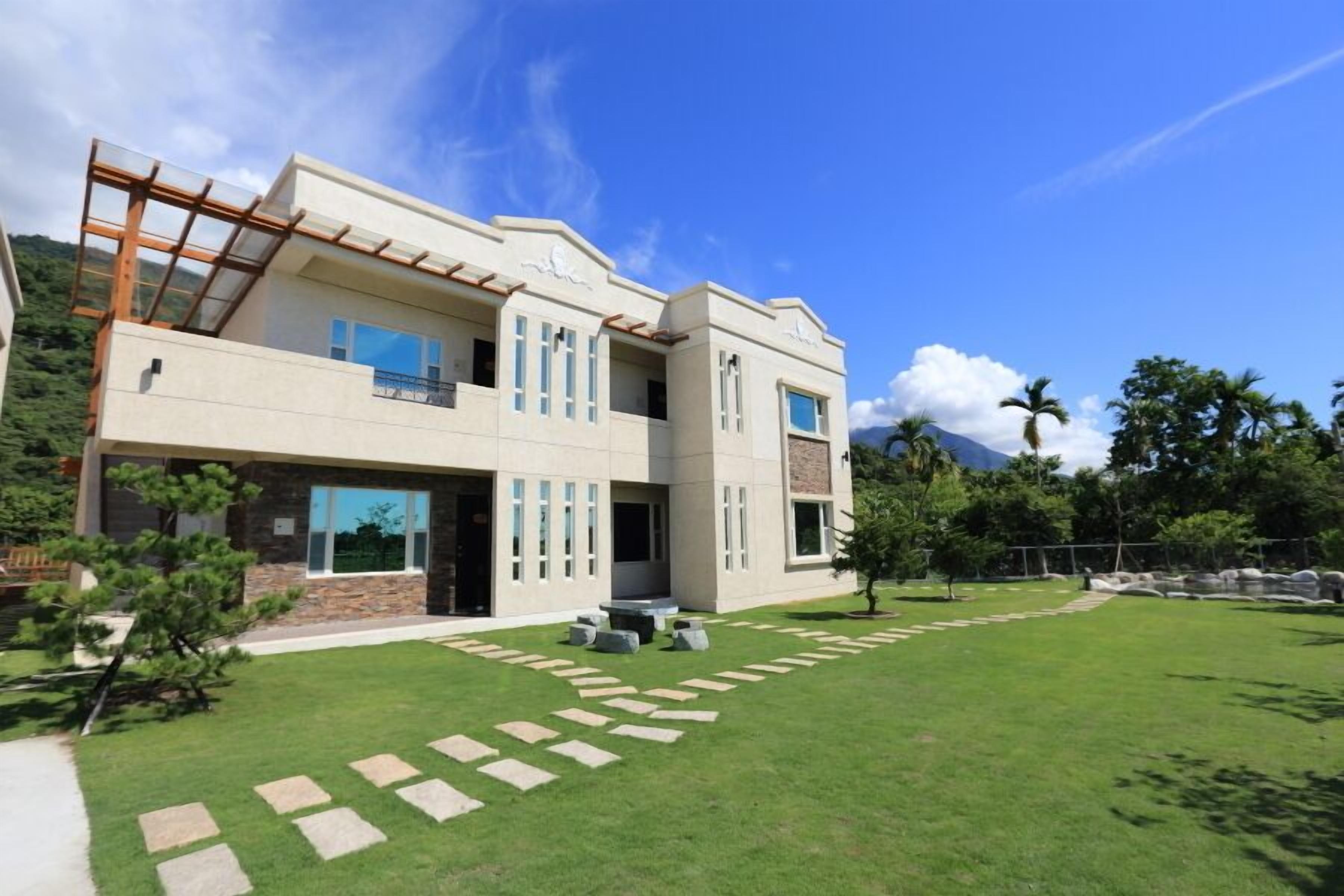 A modern two-story house with a spacious front yard, stone pathway, and a clear view of the surrounding landscape.