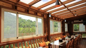 A covered outdoor dining area with wooden tables and benches, large windows, and a view of greenery. - Cai Feng B&B (Ji'an)