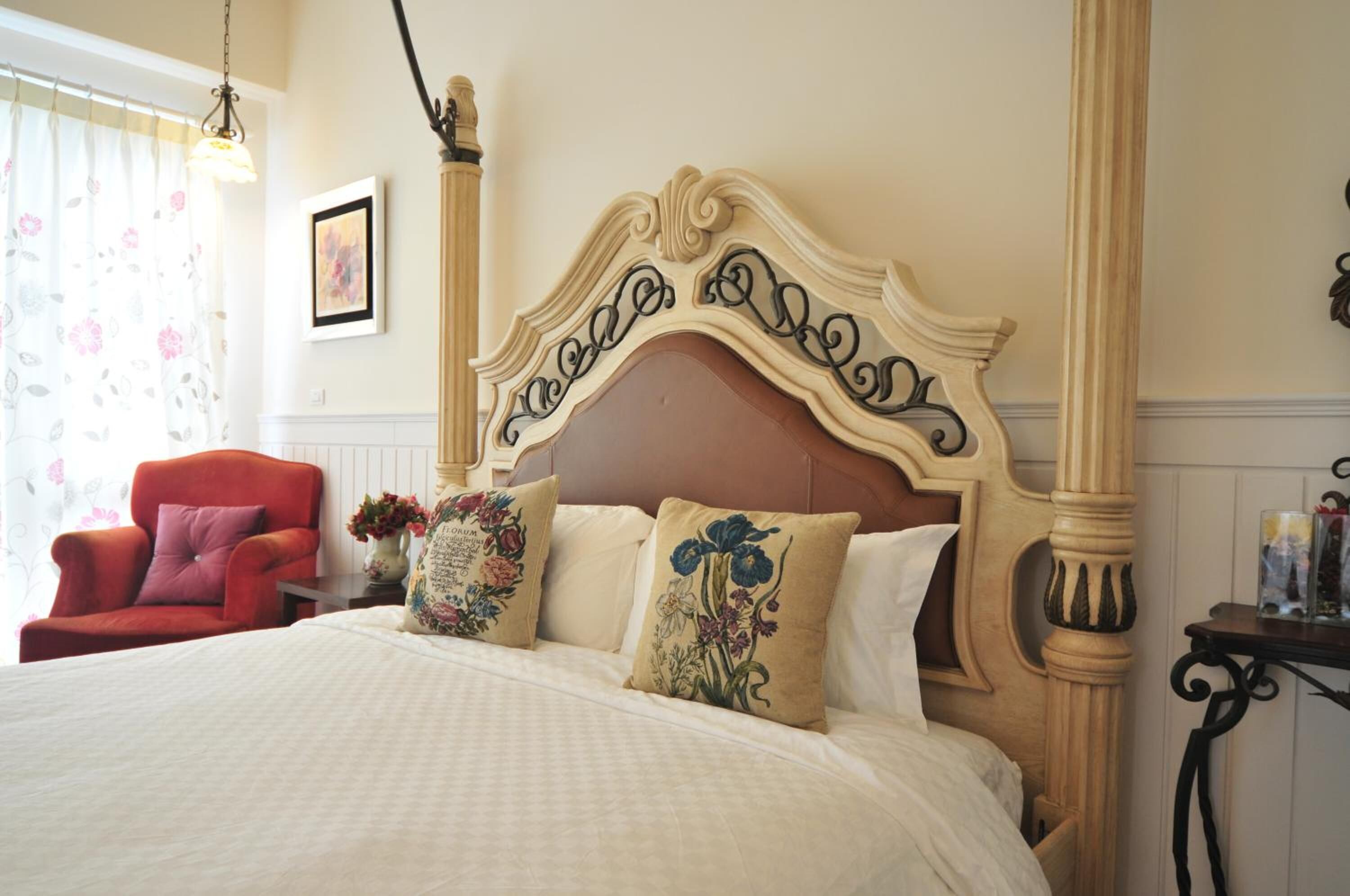 A bed with a decorative headboard, a red armchair, and a vase with flowers.
