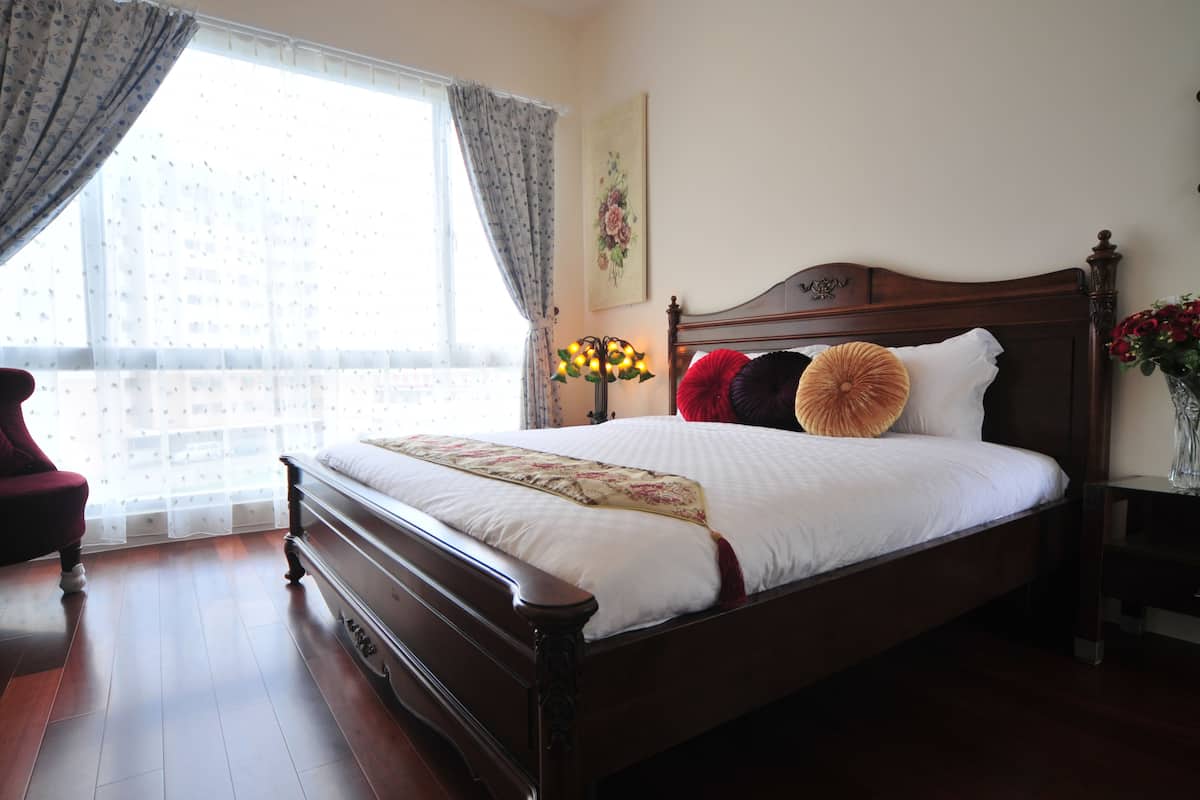 Una cama bien hecha con cabecera de madera, colcha estampada con motivos florales y almohadones decorativos.
