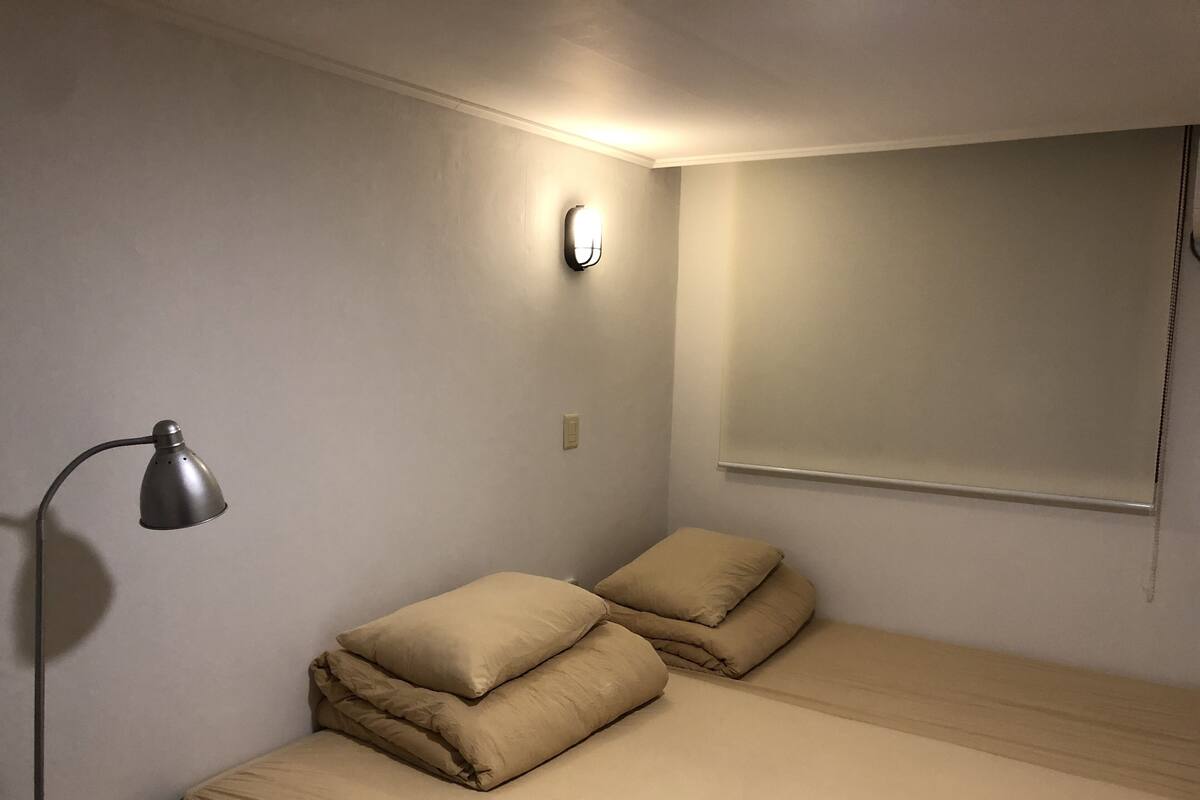 A small, dimly lit room with a single bed, a bedside lamp, and a wall-mounted light fixture.