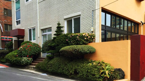 A modern building with a brick facade, large windows, and a well-maintained garden with various shrubs and flowers.