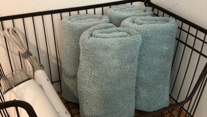 A metal basket containing several rolled-up towels and a white appliance, possibly a vacuum cleaner, on a tiled floor.