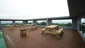 A wooden deck with picnic tables and benches overlooking a body of water. - Bowoohill (Seogwipo)