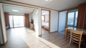 A hotel room with a large bed, a desk, a chair, and a view of the city. - Bowoohill (Seogwipo)