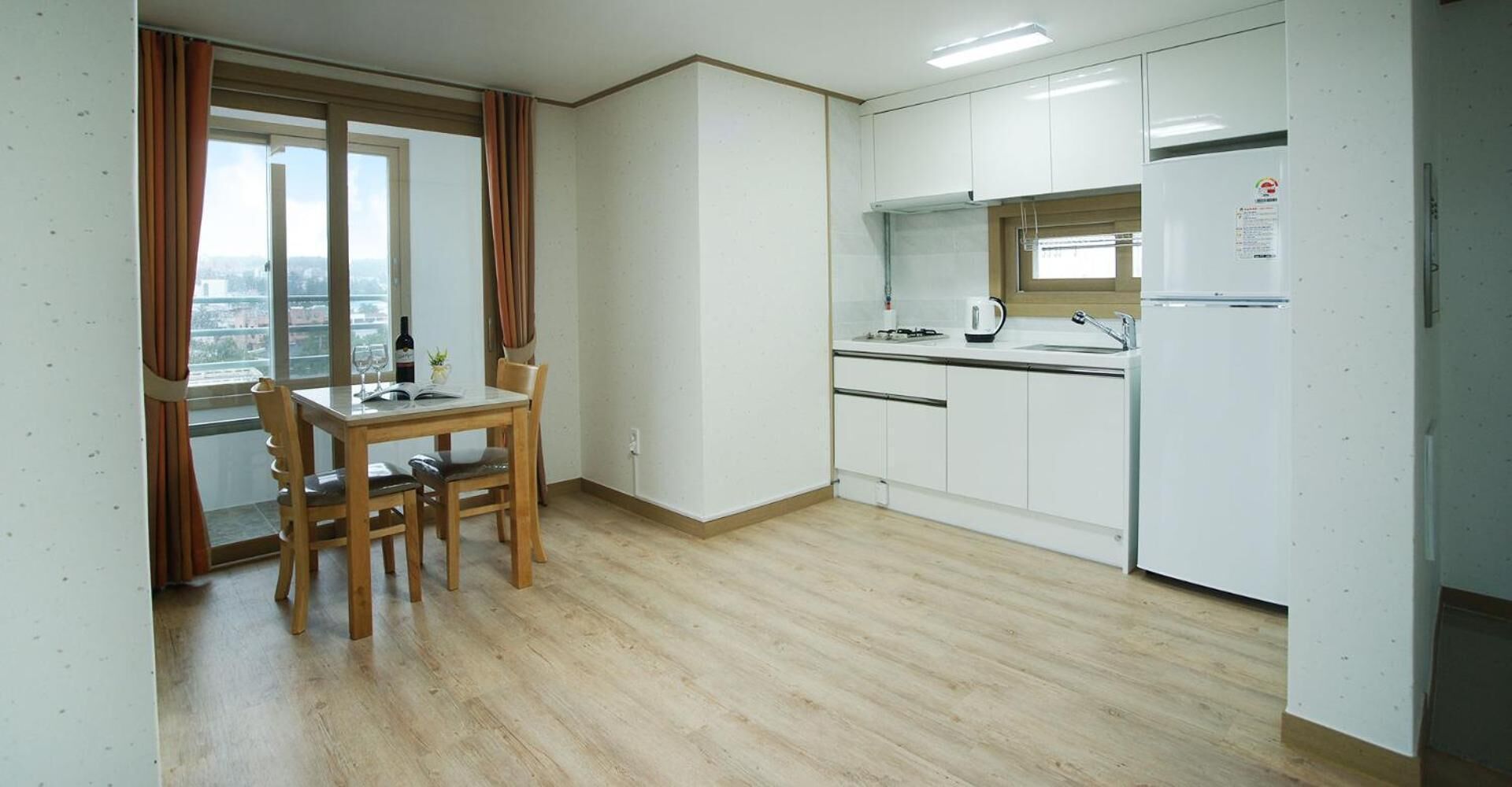 A compact kitchen with white cabinets, a dining area with a table and chairs, and a view through a window.