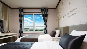 Ett hotellrum med två sängar, ett skrivbord, ett stort fönster med utsikt och en vägg med ett träd och text på.