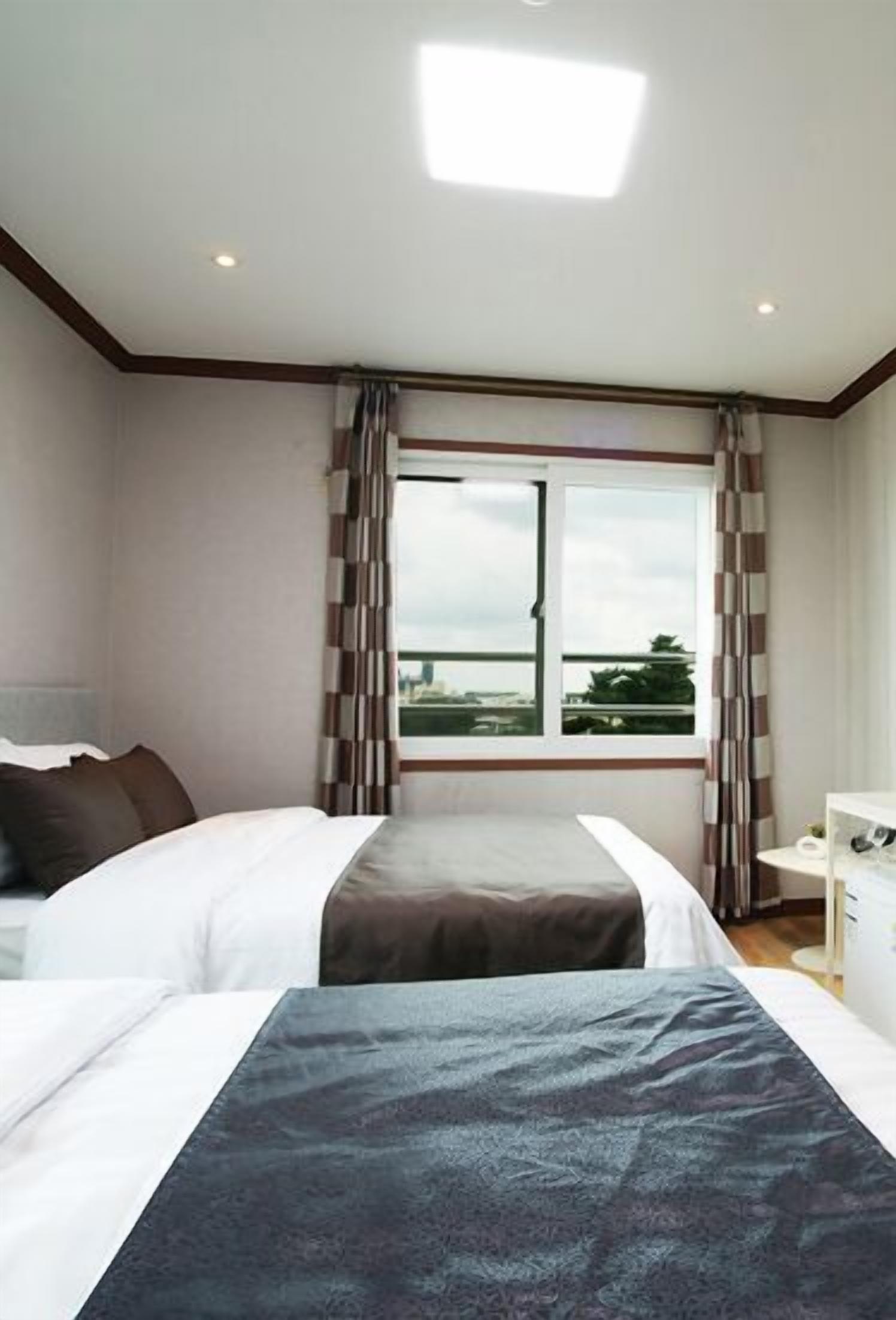 Habitación de hotel con dos camas, un ventanal con cortinas, un escritorio con silla y vista a la ciudad.