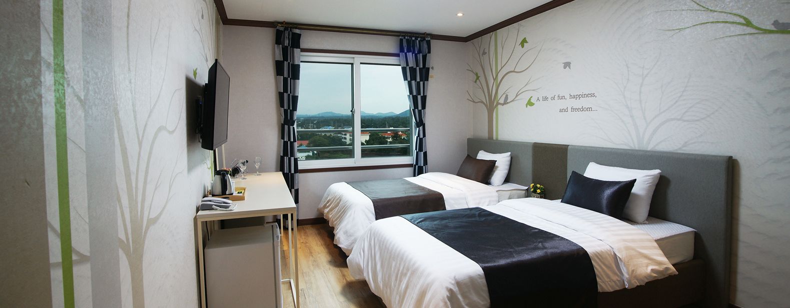 Een hotelkamer met twee bedden, een bureau, een televisie en een raam met uitzicht.