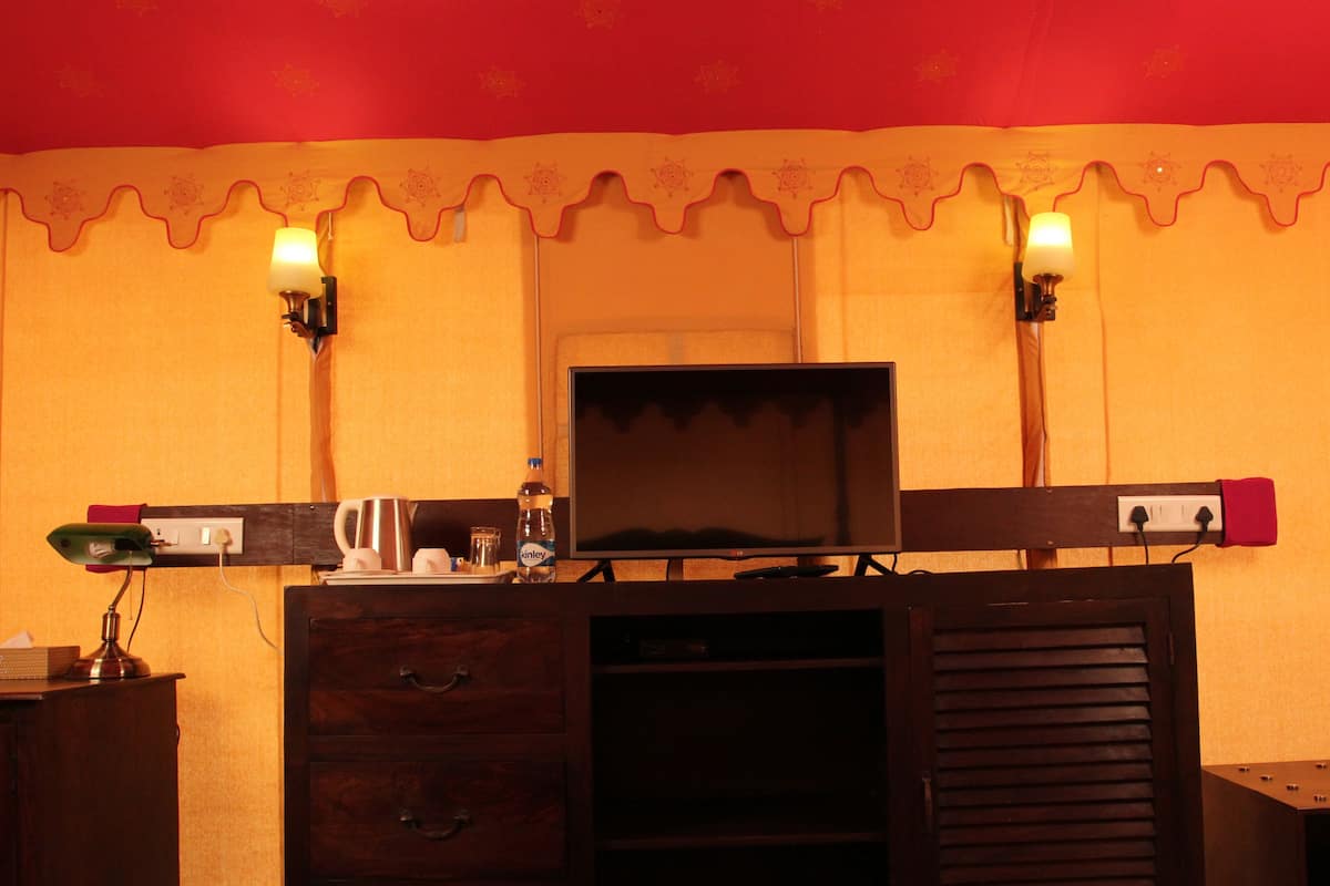 A room with a television on a wooden stand, a desk with a lamp, and two wall-mounted lights.