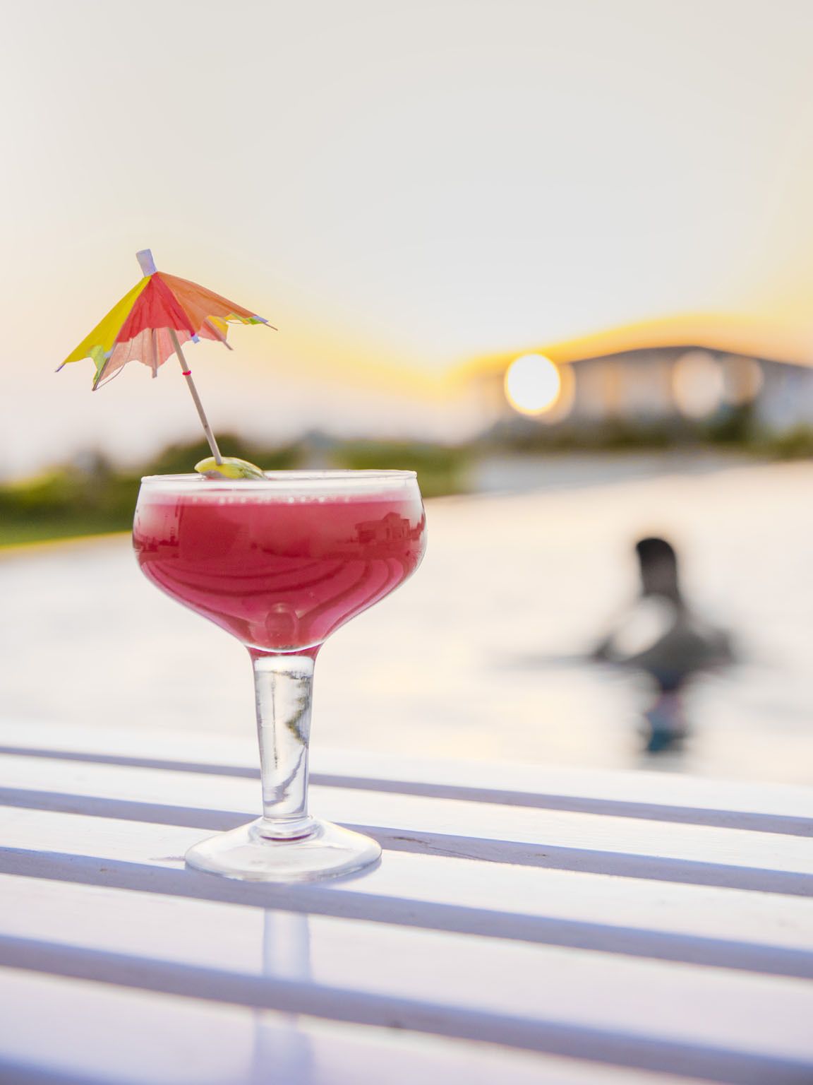 A cocktail in a glass with a colorful umbrella on a white table with a blurred background.