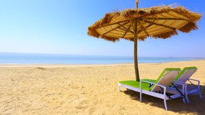 A beach with two white lounge chairs and a straw umbrella. - Serena Beach Resort (Mandvi)