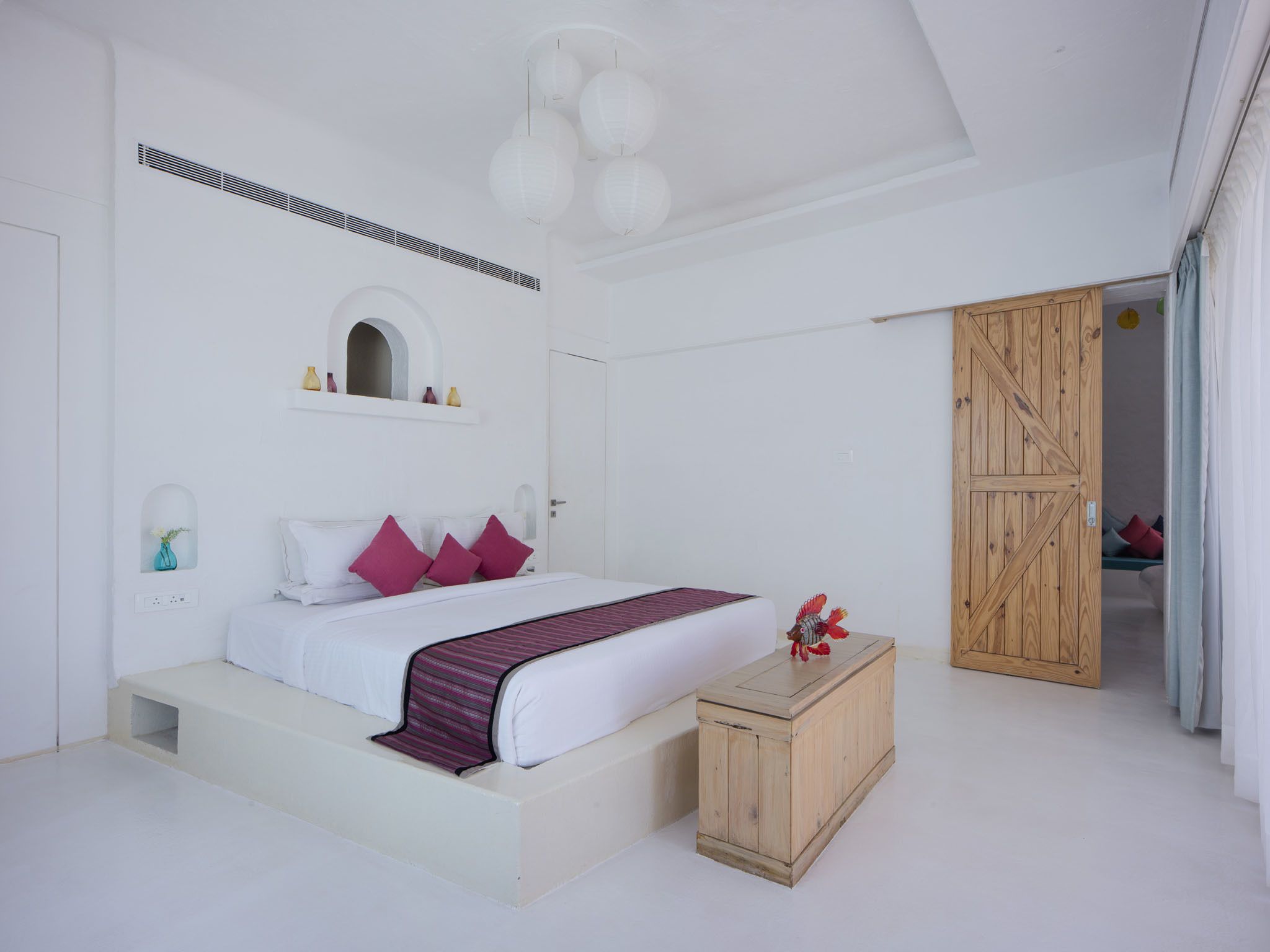 A bedroom with a bed, bedside tables, a wardrobe, and a door leading to another room.