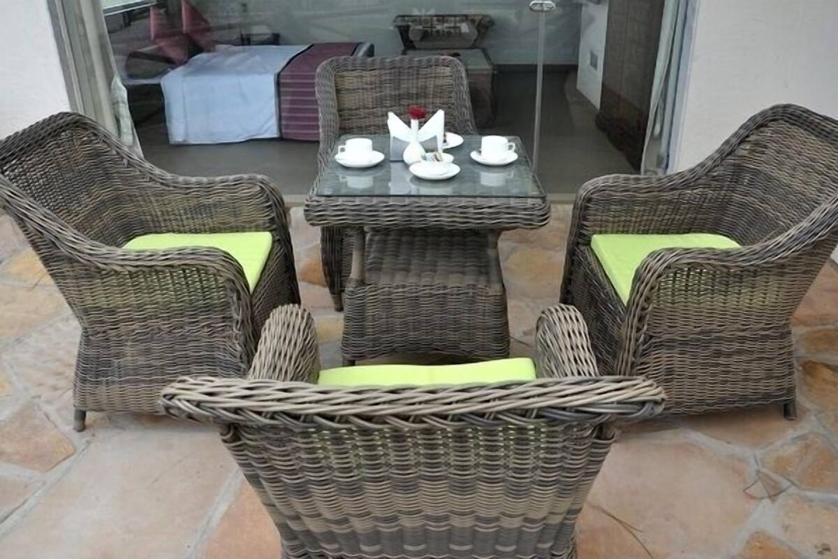 A wicker dining set with a glass table and chairs, a white vase with a red flower, and a white table runner.