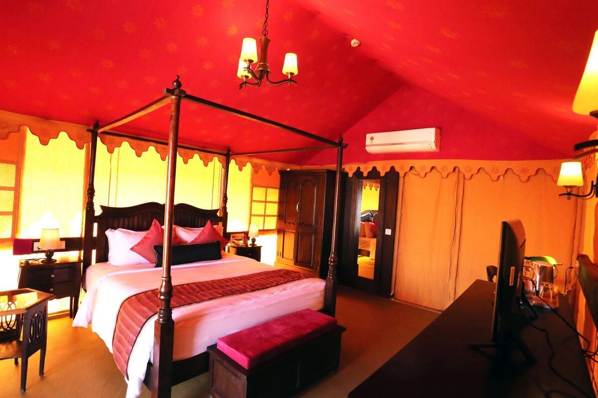 A four-poster bed with a canopy, bedside tables, a desk with a computer, and an air conditioning unit.