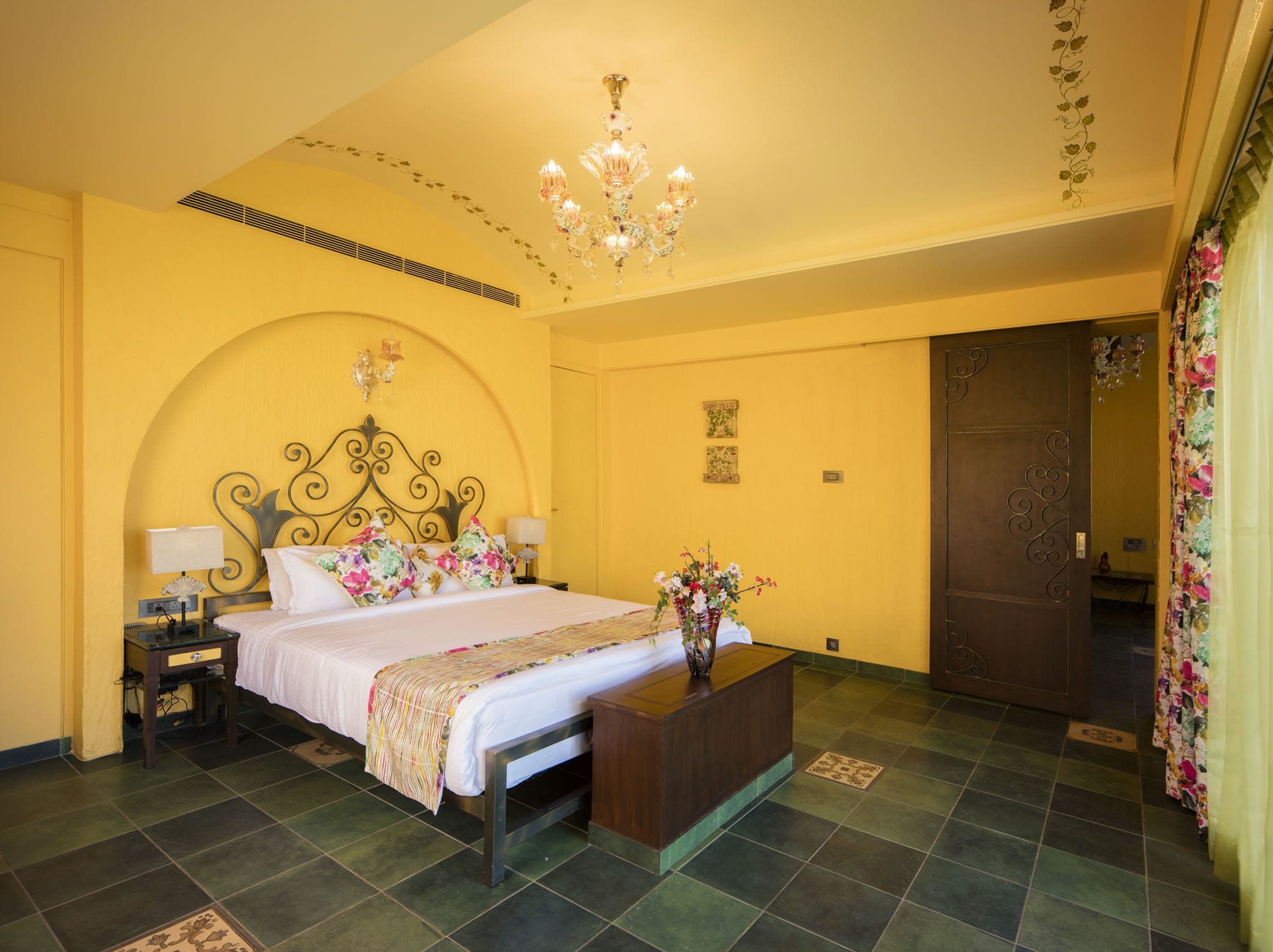 Une chambre d’hôtel avec un lit, des tables de chevet, un bureau, un lustre et une porte.