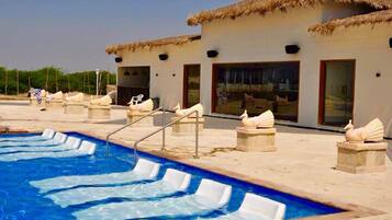 A pool area with lounge chairs and a building with a thatched roof.
