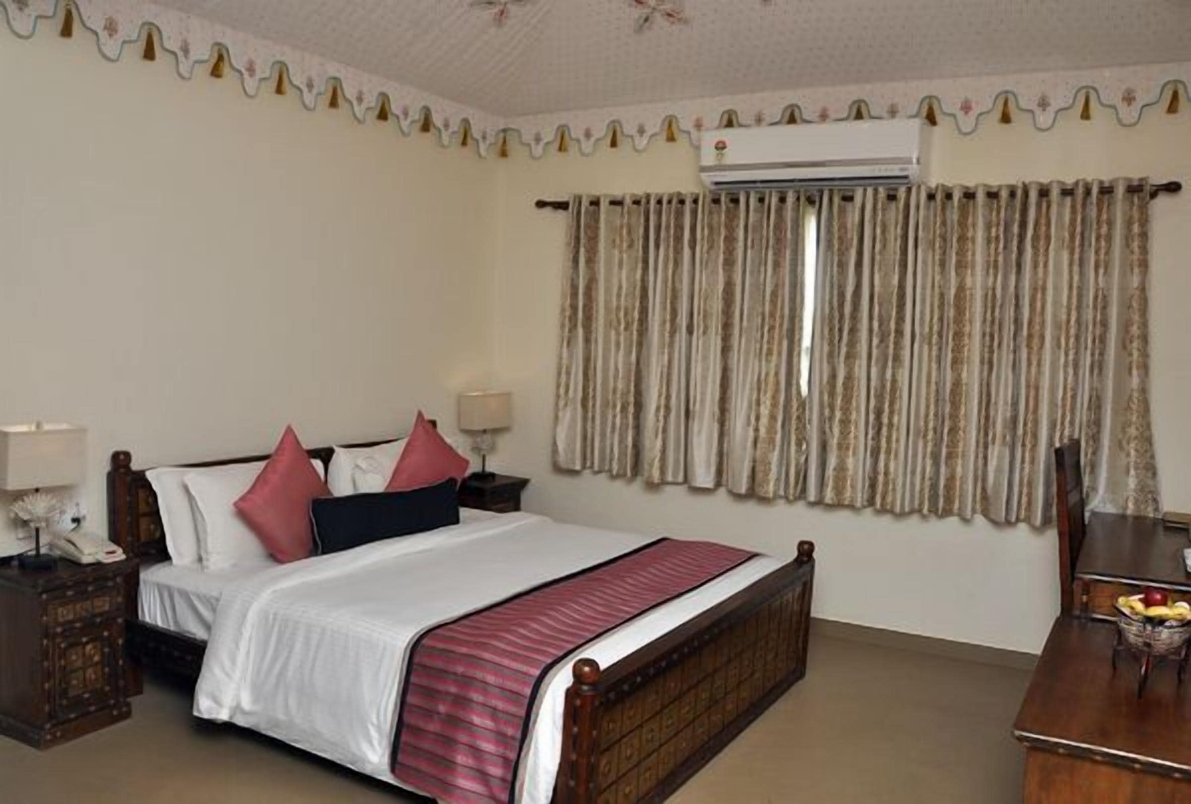 A bedroom with a bed, bedside tables, an air conditioning unit, and a dining table with fruit.