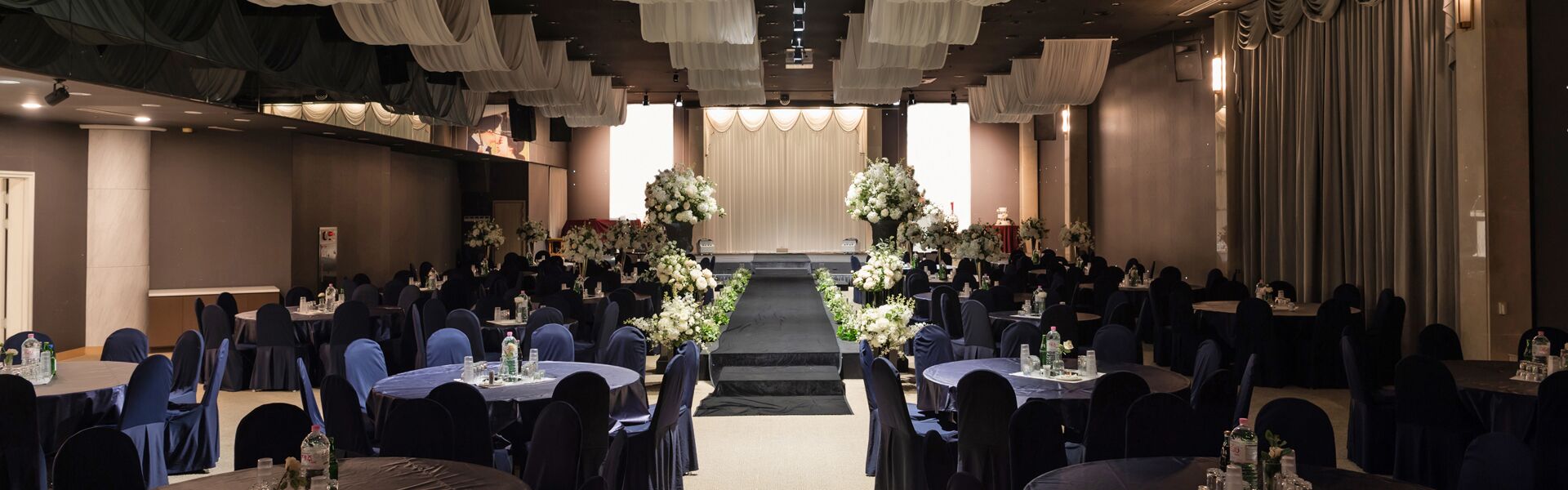 A banquet hall with round tables, blue chairs, and floral centerpieces.