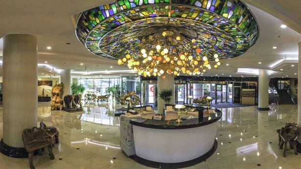 Eine geräumige Lobby mit einer zentralen Rezeption, einer großen Glasdecke im Stil des Jugendstils und einem polierten Boden.