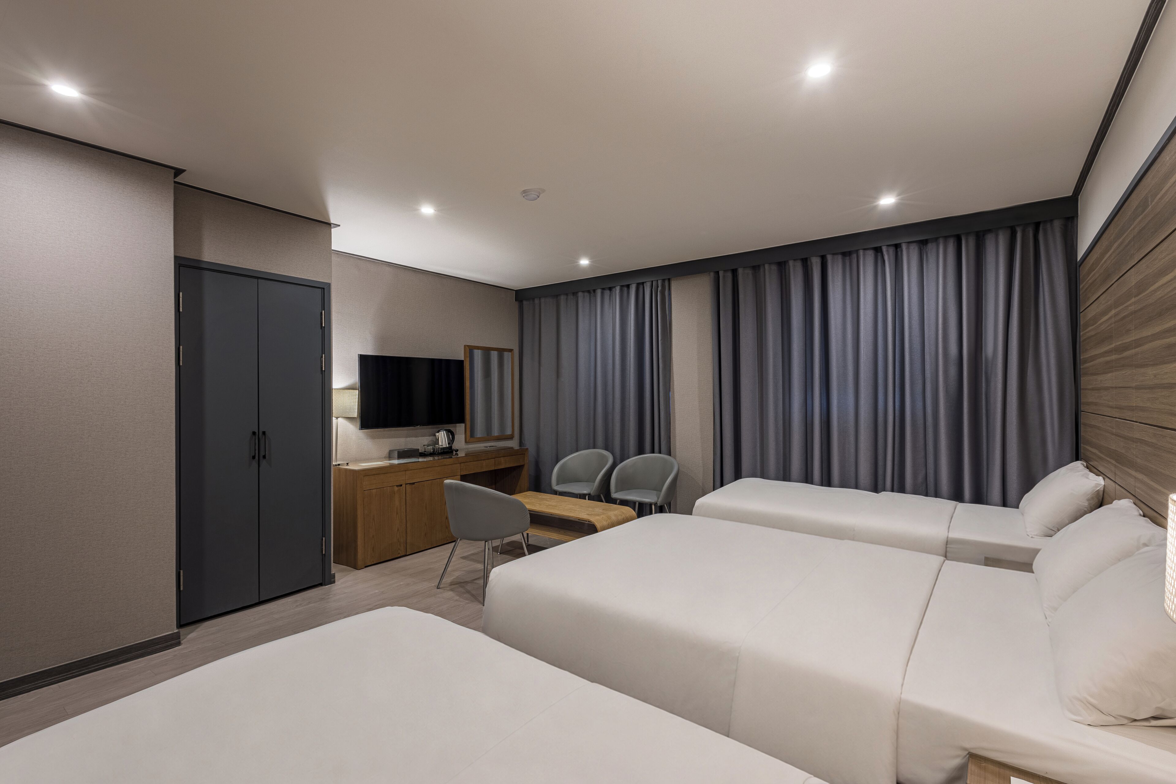 Quarto de hotel com duas camas, uma escrivaninha com cadeira, televisão e guarda-roupa.