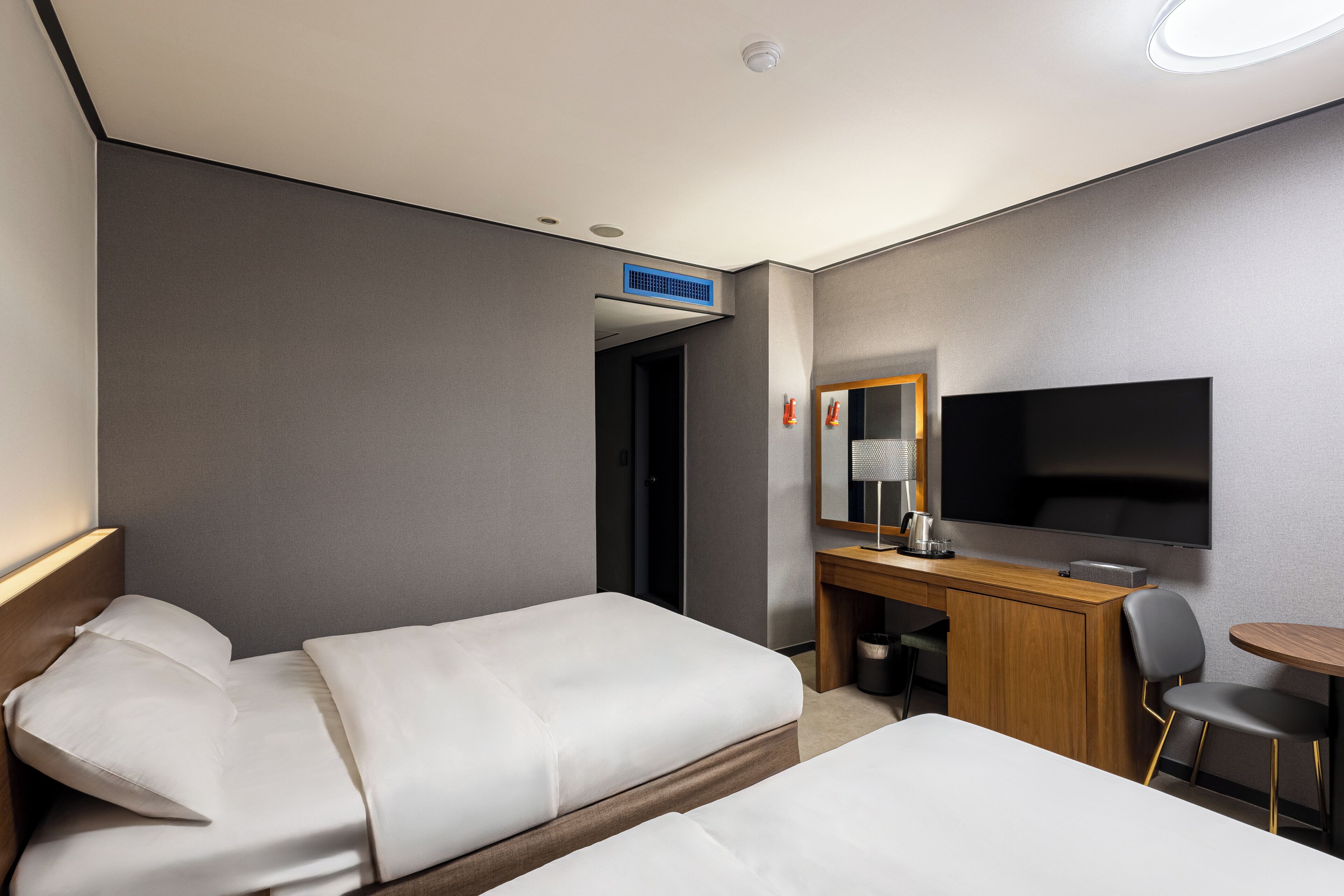 Una habitación de hotel con dos camas, un escritorio, una silla, un televisor y un espejo.