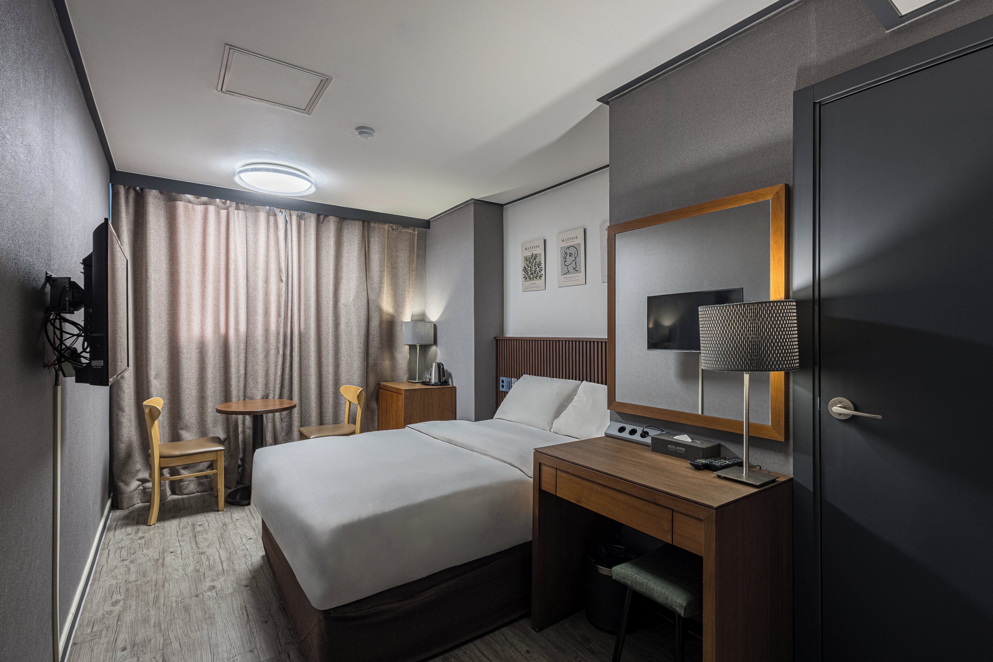 A hotel room with a bed, a desk, a chair, a television, and a door.