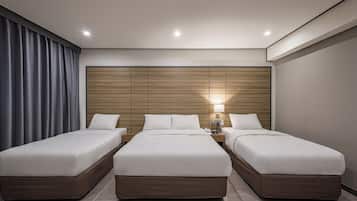 Une chambre d’hôtel avec trois lits, une tête de lit en bois, une table de chevet avec une lampe et une grande fenêtre avec des rideaux.