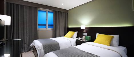 Habitación de hotel con dos camas, un escritorio, una lámpara y una ventana con cortinas.
