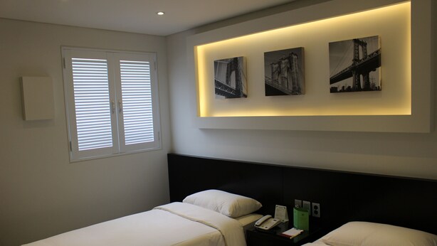 Habitación de hotel con dos camas, una ventana con persianas y tres cuadros en la pared.