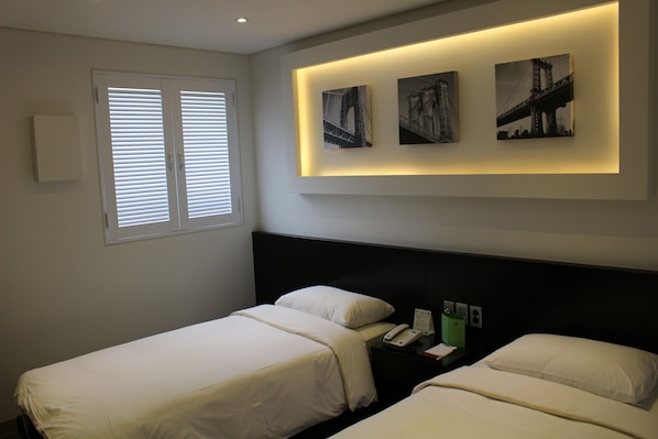 A hotel room with two beds, a window with blinds, and three framed pictures on the wall. - Insadong Crown Hotel (Seoul)