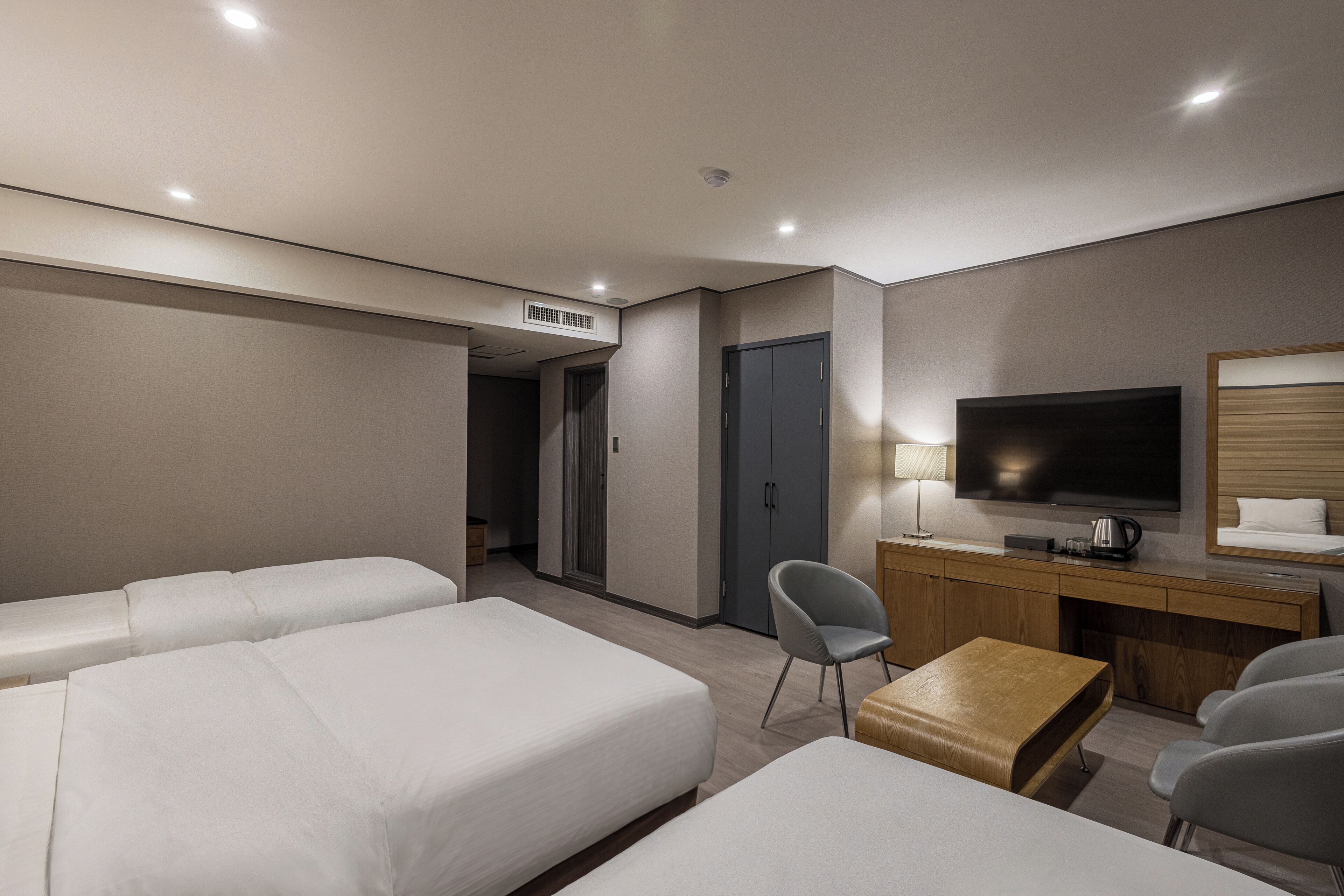 A hotel room with two beds, a desk, a chair, a television, and a small table.